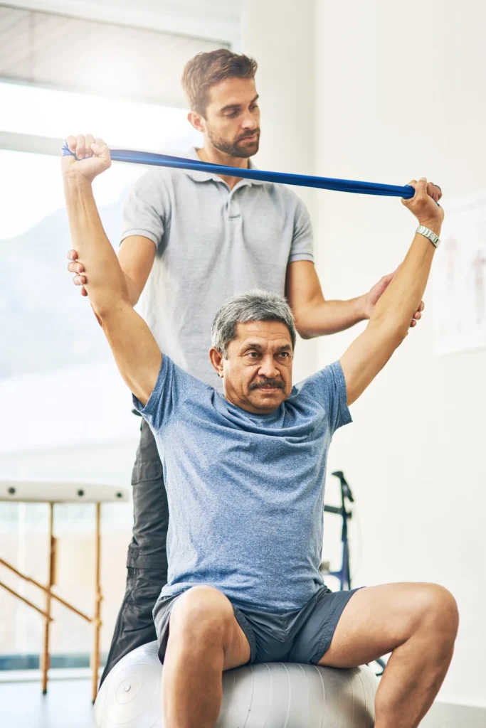 Physiotherapist assisting elderly man with resistance band exercises on a therapy ball